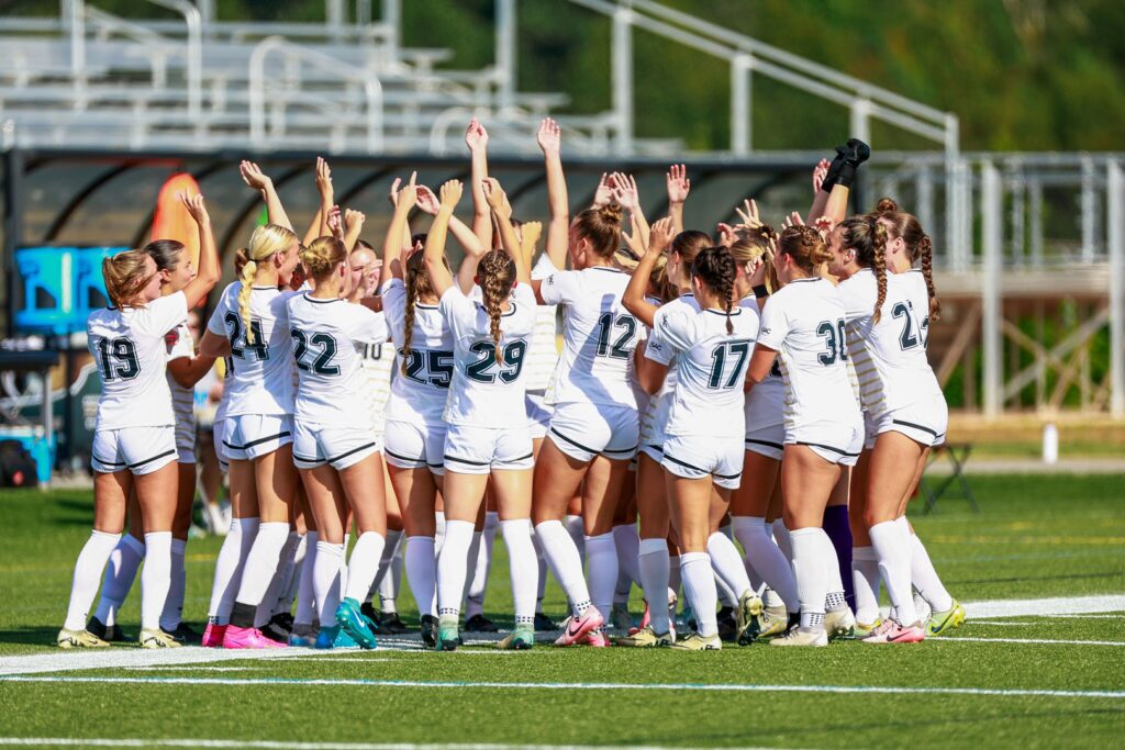 Team of female soccer players in a huddle with arms raised on a field.