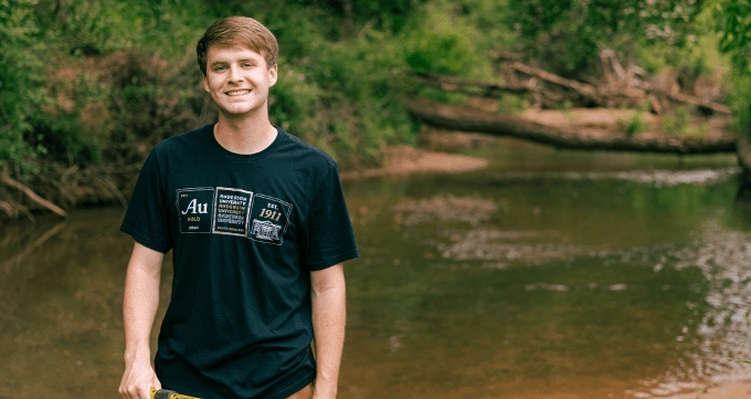 Student in the woods standing by a river