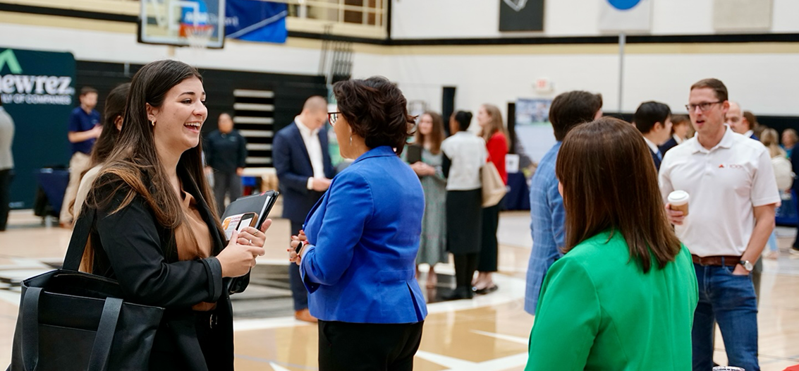 Job recruiters standing in a gym talking with students.
