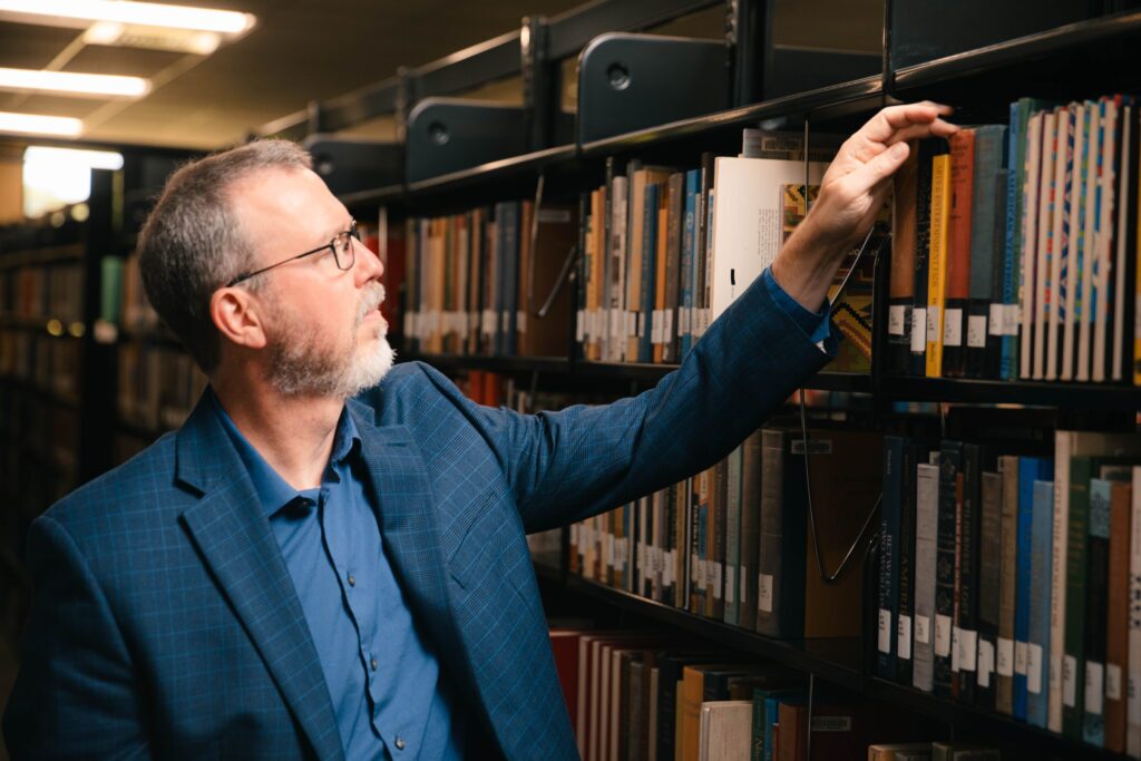 Professor Cox in Anderson University's library looking at a shelf full of books
