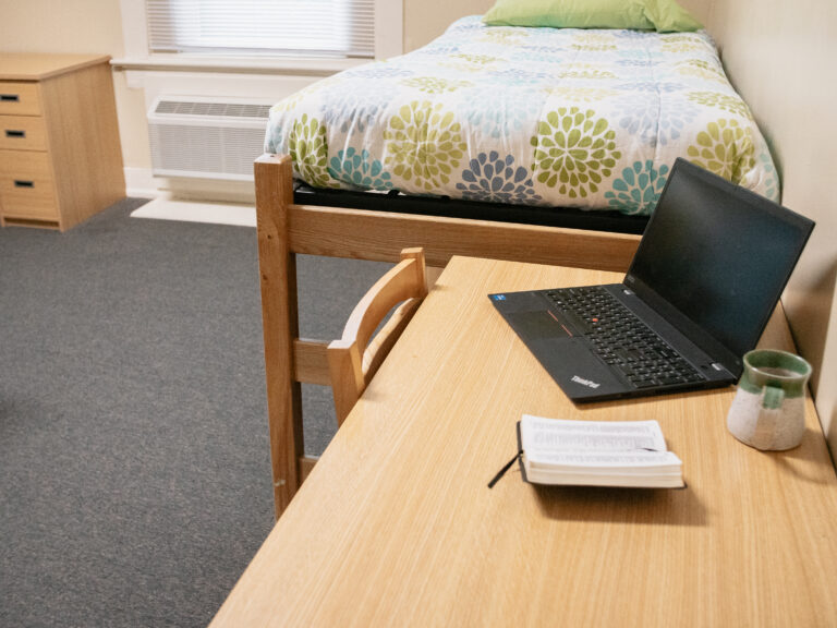 Pratt Denmark Suite Residence Halls bedroom desk with laptop, coffee mug, and bible