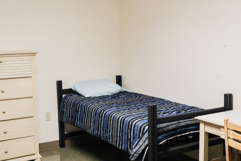 Village Basement Community Residence bedroom with bed, desk, and cabinet